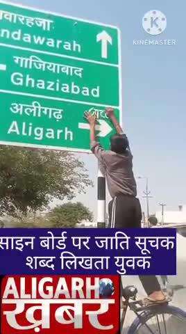 हाईवे किनारे बने साइन बोर्ड पर अलीगढ़ की दिशा दिखाने वाले एंरो पर जाति सूचक शब्द लिखता युवक